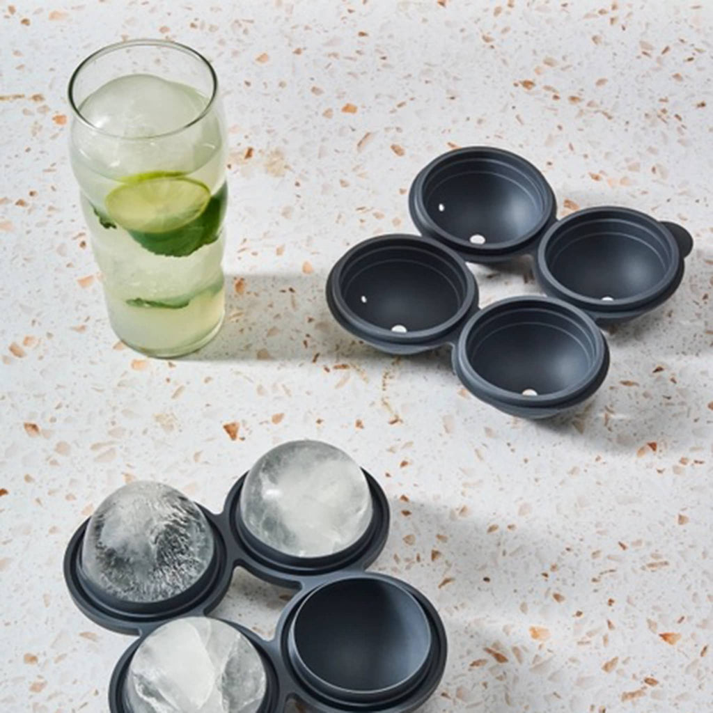 W&P Design Sphere Ice Tray Quad in charcoal gray, open with ice inside and a glass with a beverage and round ice inside.