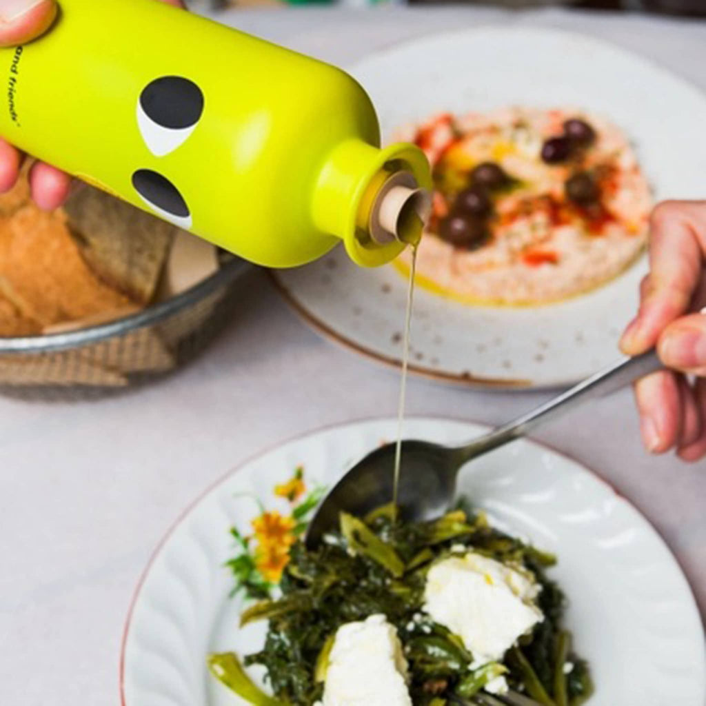 yiayia and friends lemon infused greek extra virgin olive oil in yellow glass bottle with eyes, being poured over a salad.