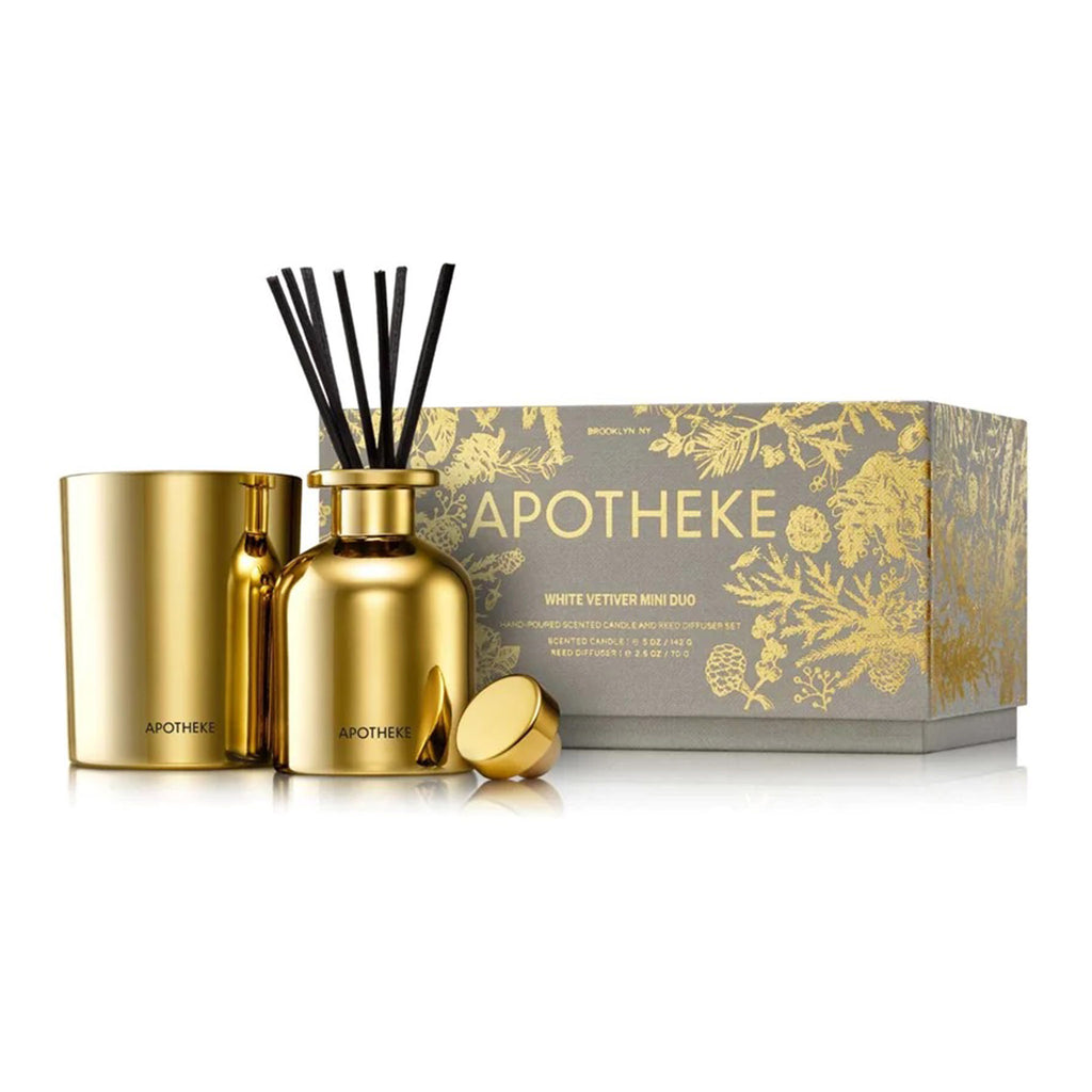 Apotheke White Vetiver Scented Mini Duo limited edition holiday gift set with a mini candle and reed diffuser, both in shiny gold glass vessels. Packaged in a grey gift box with gold foil tree branch illustrations.