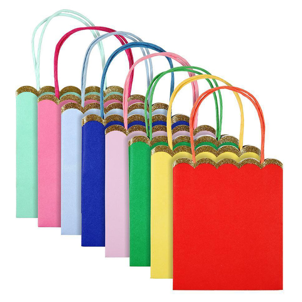 Pack of 8 party bags in solid rainbow colors, top edge is scalloped and has a gold glitter trim, raffia handles match the bag colors. Colors from left to right: mint green, dark pink, light blue, royal blue, light pink, green, yellow and red.