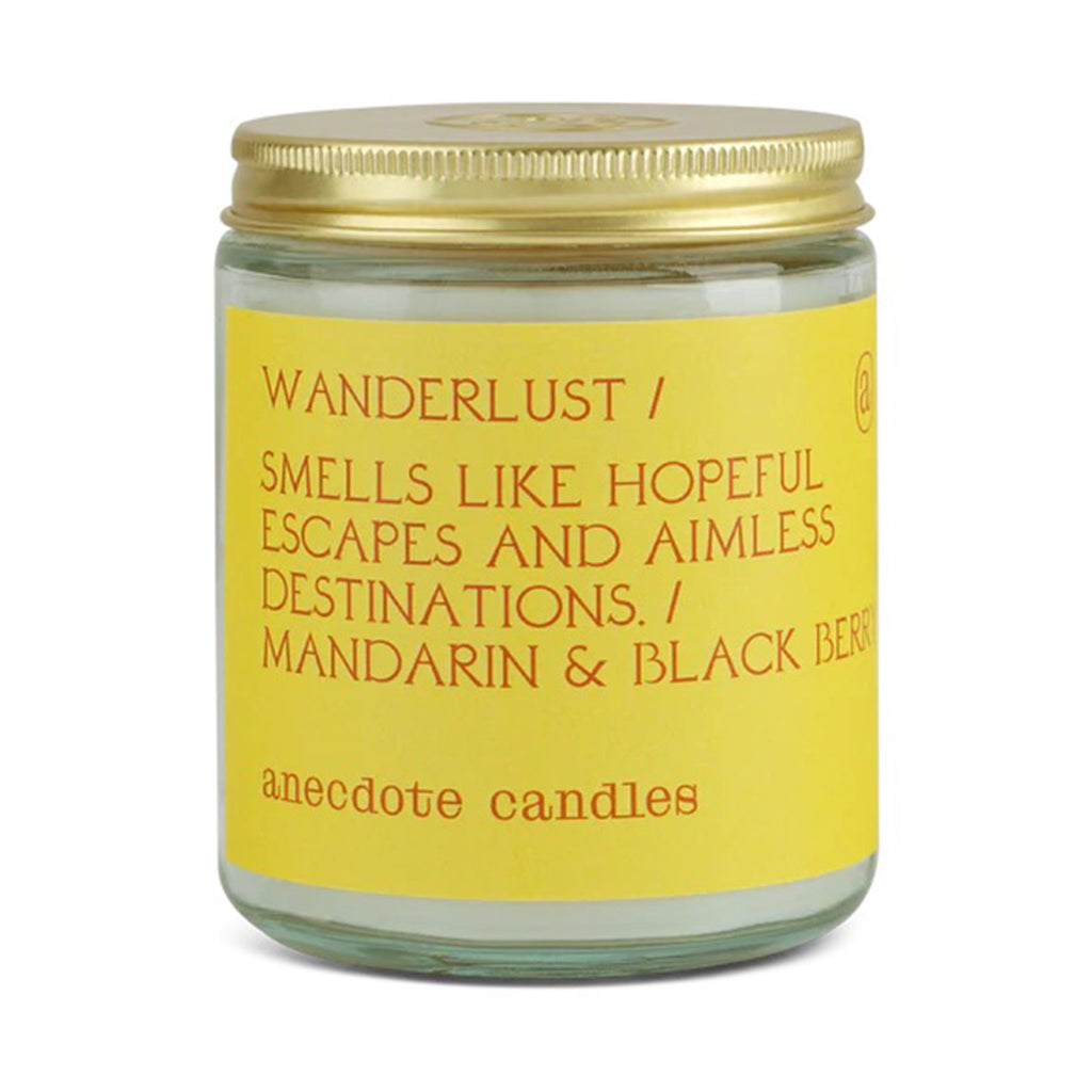anecdote wanderlust mandarin and black berry scented coconut soy wax blend candle in a clear glass jar with screw on gold lid and yellow label with orange writing
