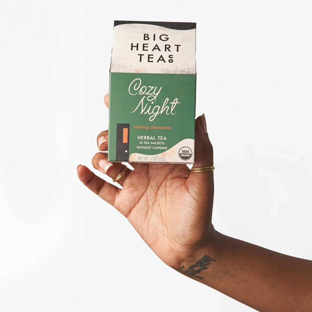 Big heart company cozy night herbal tea bags packaged in box that looks like a green house, being held in an outstretched hand.