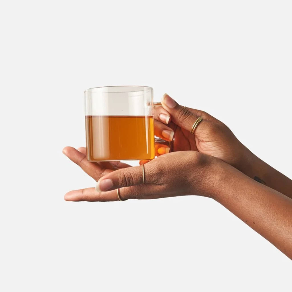 Winter chai brewed in clear glass mug, being held by the handle and underneath by hands.