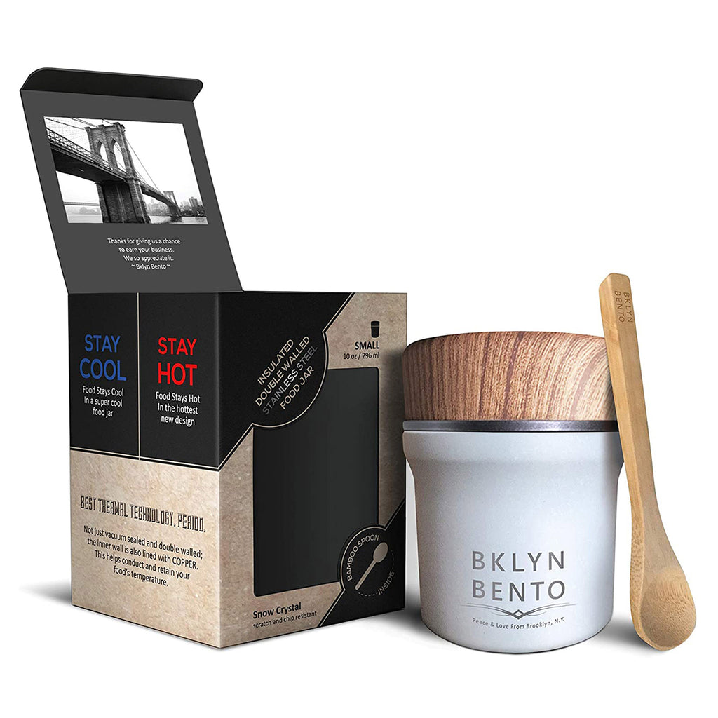 White stainless steel insulated food jar with faux wood lid, a bamboo spoon is propped up against the jar and it's beside the tan and black paper box it comes in.