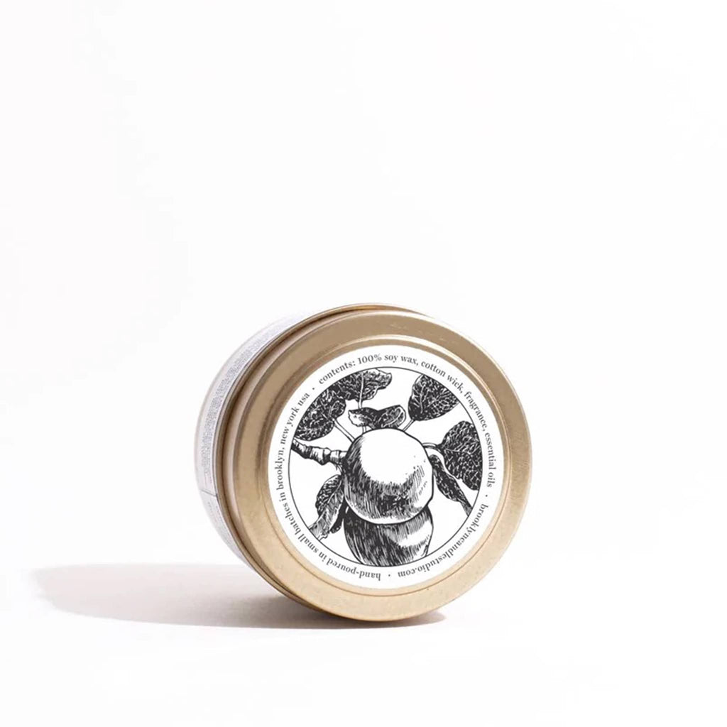 Apple Cider scented candle in brushed gold travel tin sitting on its side to show an apple on a tree illustration on the top of the lid.