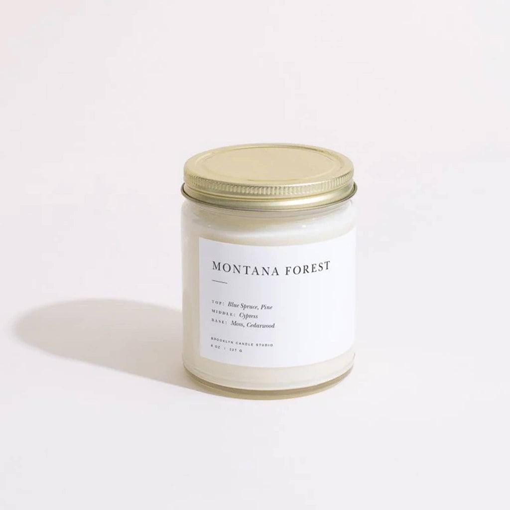 Montana Forest scented candle in a straight sided clear glass jar with minimalist label and brushed gold screw-on lid.