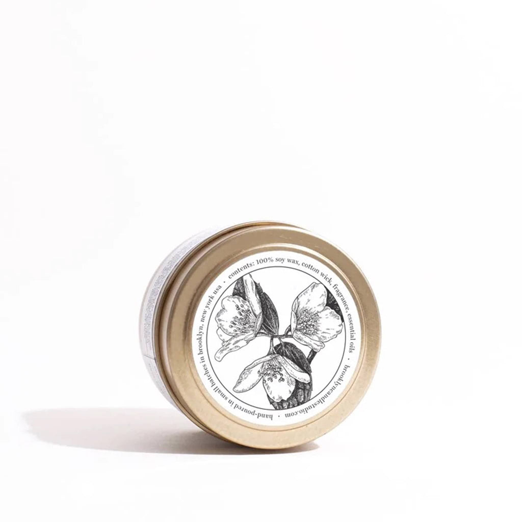 Sunday Morning scented candle in brushed gold travel tin, sitting on its side to show illustration on top of the lid.