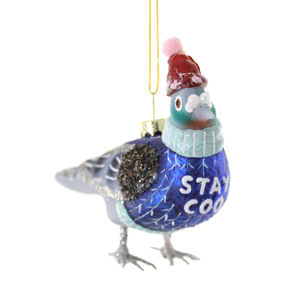 Glass pigeon ornament wearing a red hat with pink pompom and a blue sweater with "stay coo" in glittery white lettering.
