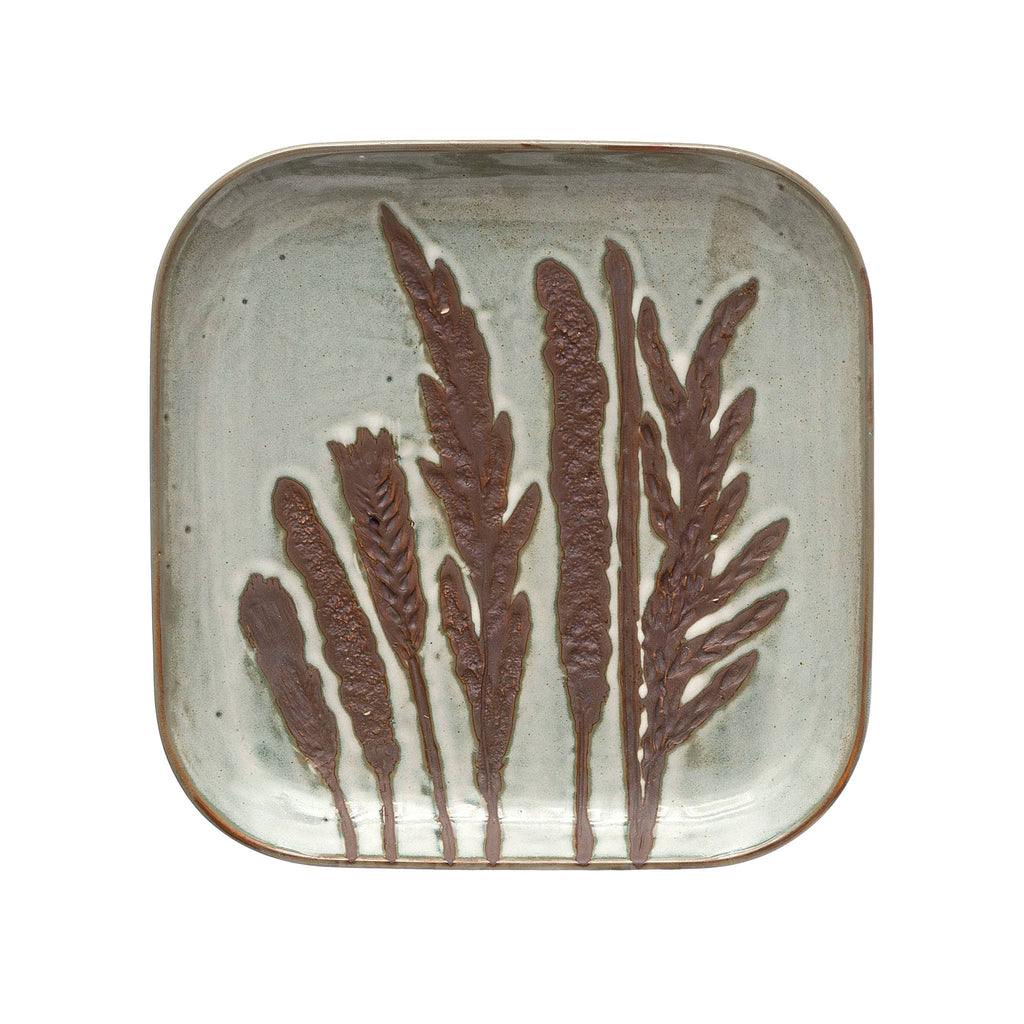 Square hand-painted debossed stoneware plate with cream color reactive glaze and an image of stems and flowers in wax relief.