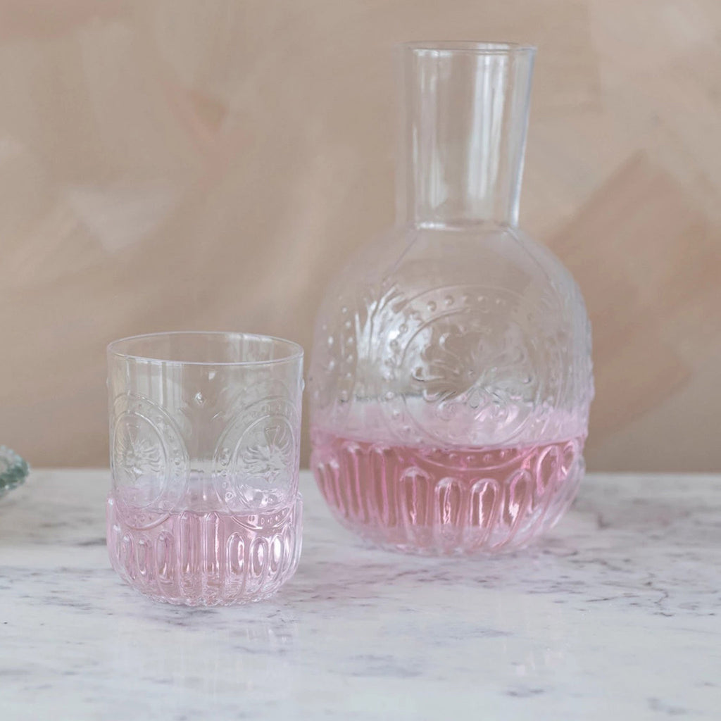 Creative Co-op 28 ounce Embossed Glass Carafe with matching 8 ounce embossed drinking glass, both are half-filled with pale pink liquid.