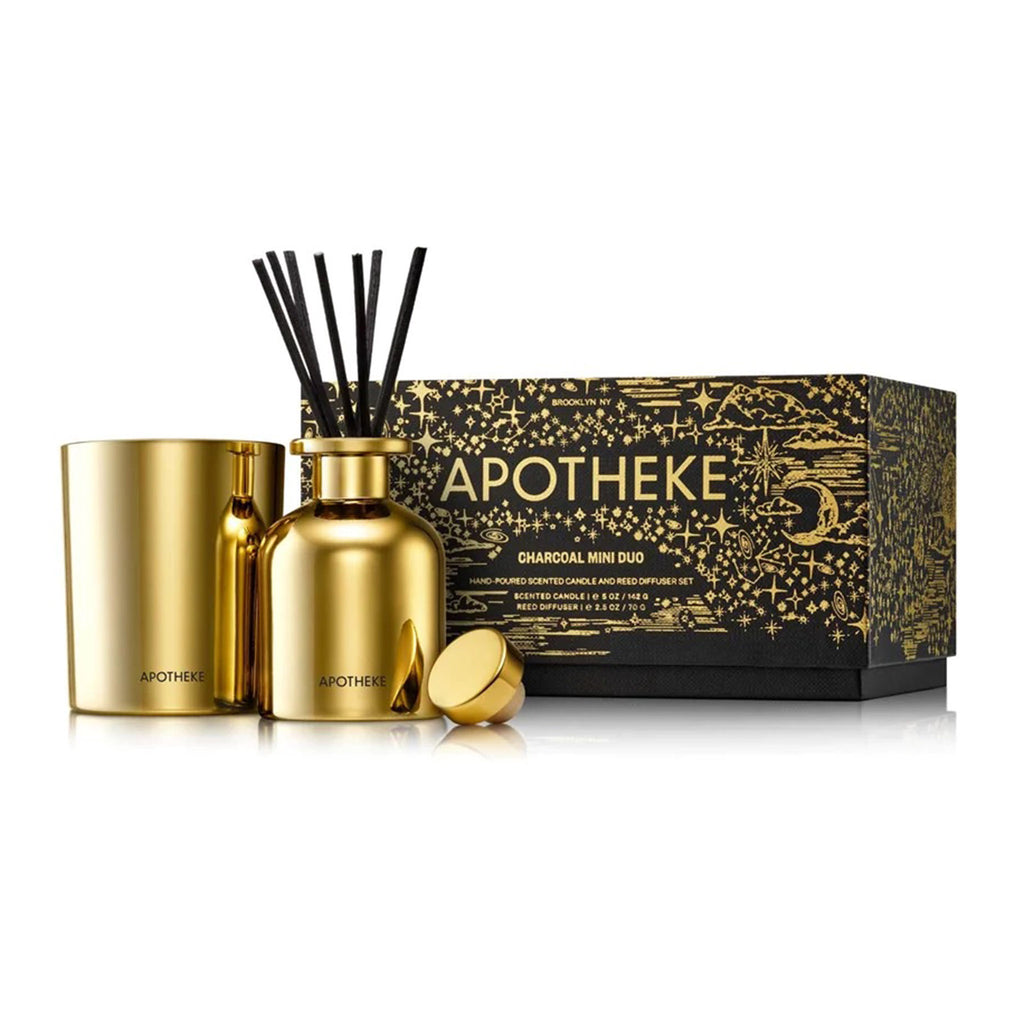 Apotheke Charcoal Scented Mini Duo limited edition holiday gift set with a mini candle and reed diffuser, both in shiny gold glass vessels. Packaged in a black gift box with gold foil constellation illustrations.