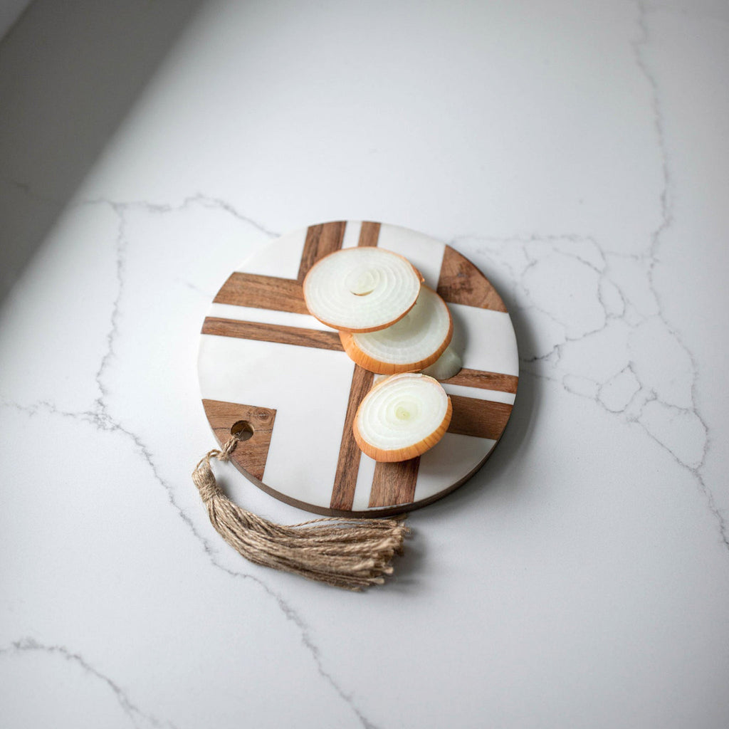 top of foreside clement small round serving board with white resin inlay in geometric pattern on acacia wood with jute tassel on white marble surface with sliced onions on board
