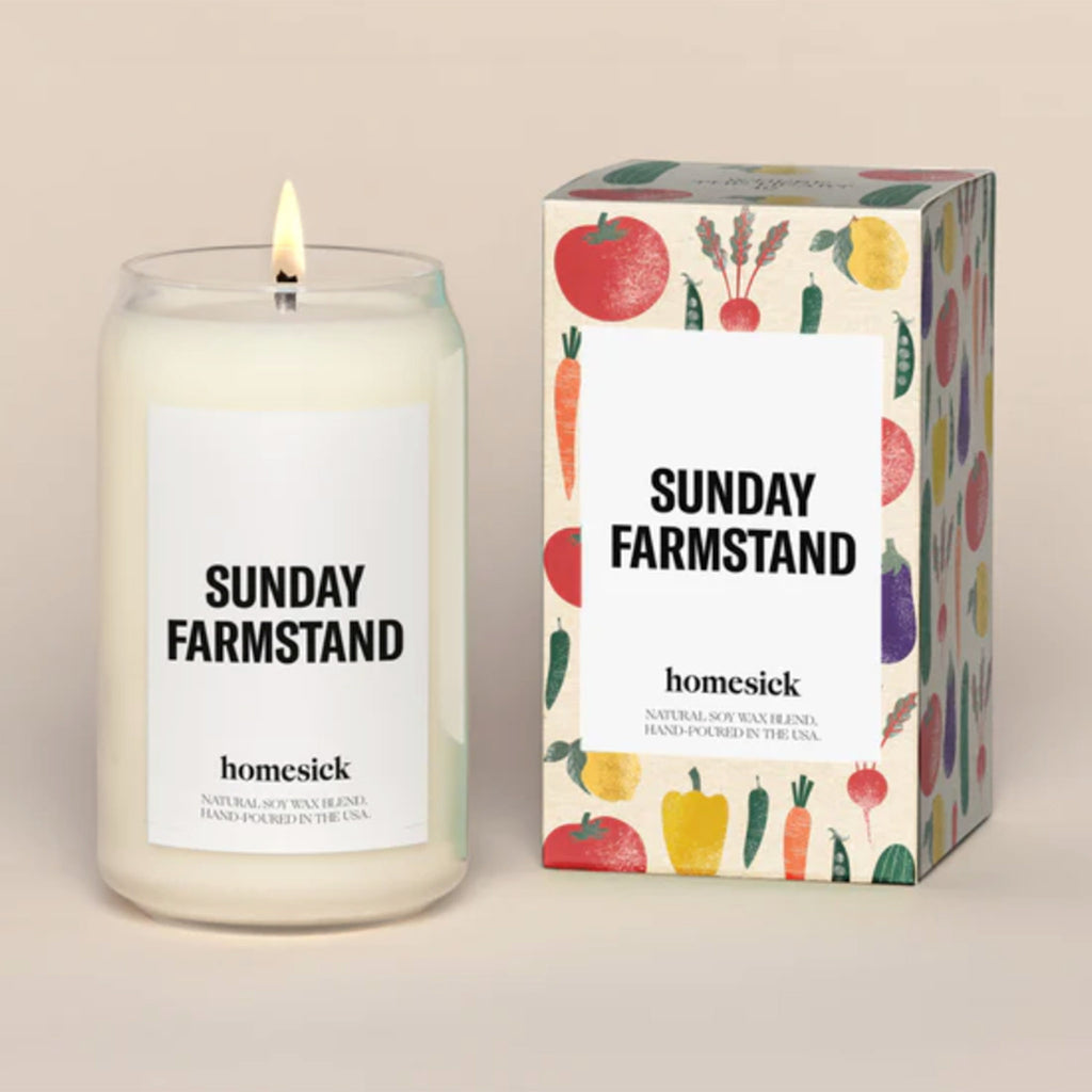 Homesick Sunday Farmstand scented candle in a can-shaped glass vessel beside gift box with fruit and vegetable illustrations.