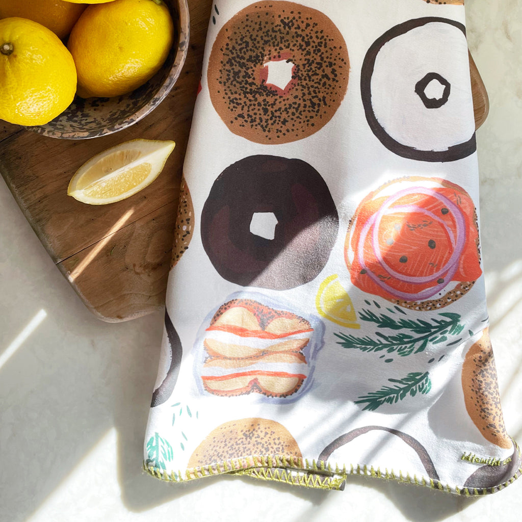Idlewild Bagels Tea Towel on a wood board with a bowl of lemons and a lemon wedge.