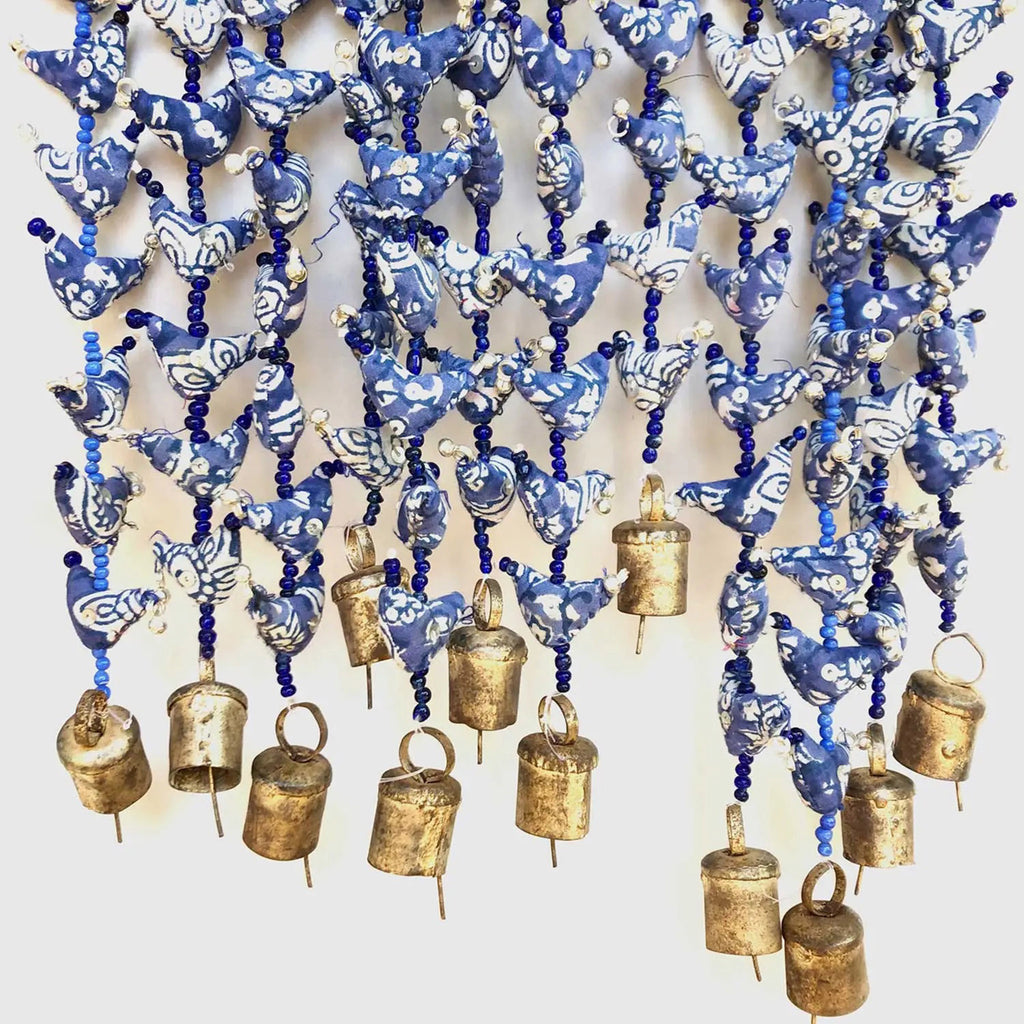 indika prosperity hen strands with blue and white small hens crafted from fabric scraps strung with blue glass beads in between and a hand formed bronze bell at the bottom.
