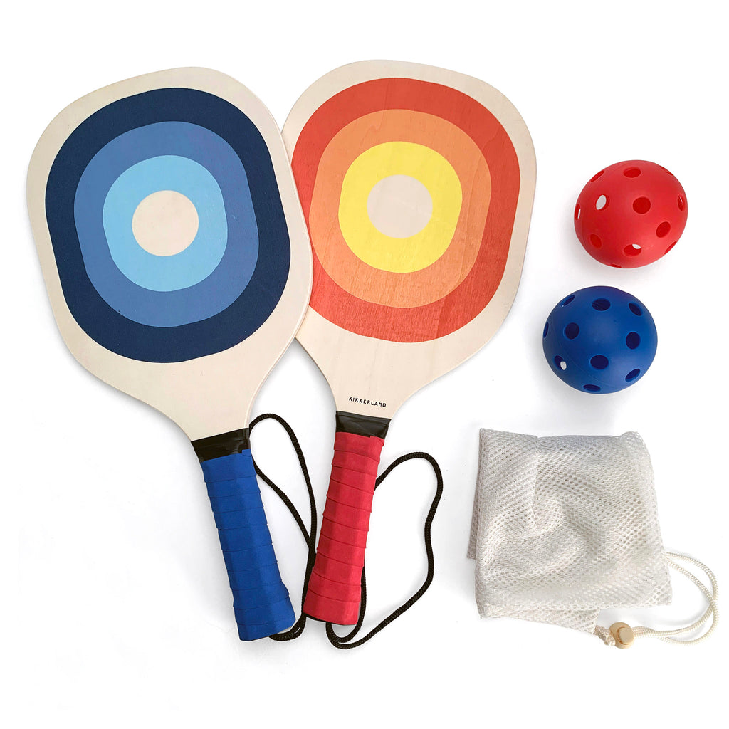 Kikkerland Pickleball Set contents, including a blue patterned paddle, a red patterned paddle, a blue ball, a red ball and a mesh travel bag.