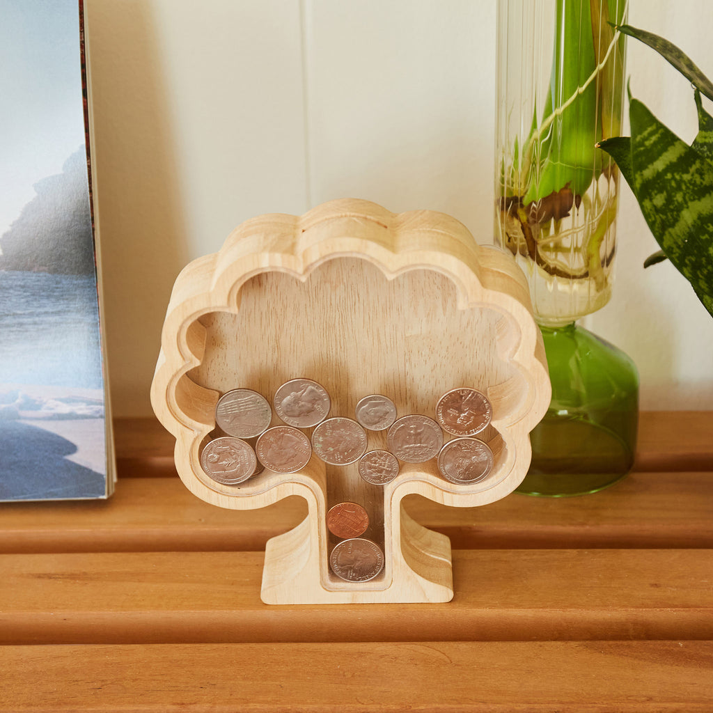 Kikkerland Money Tree wood savings bank with coins inside on a table.