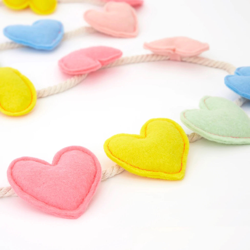 Meri Meri puffy felt hearts with neon coral stitching in pastel colors attached to a natural color braided cord, detail.