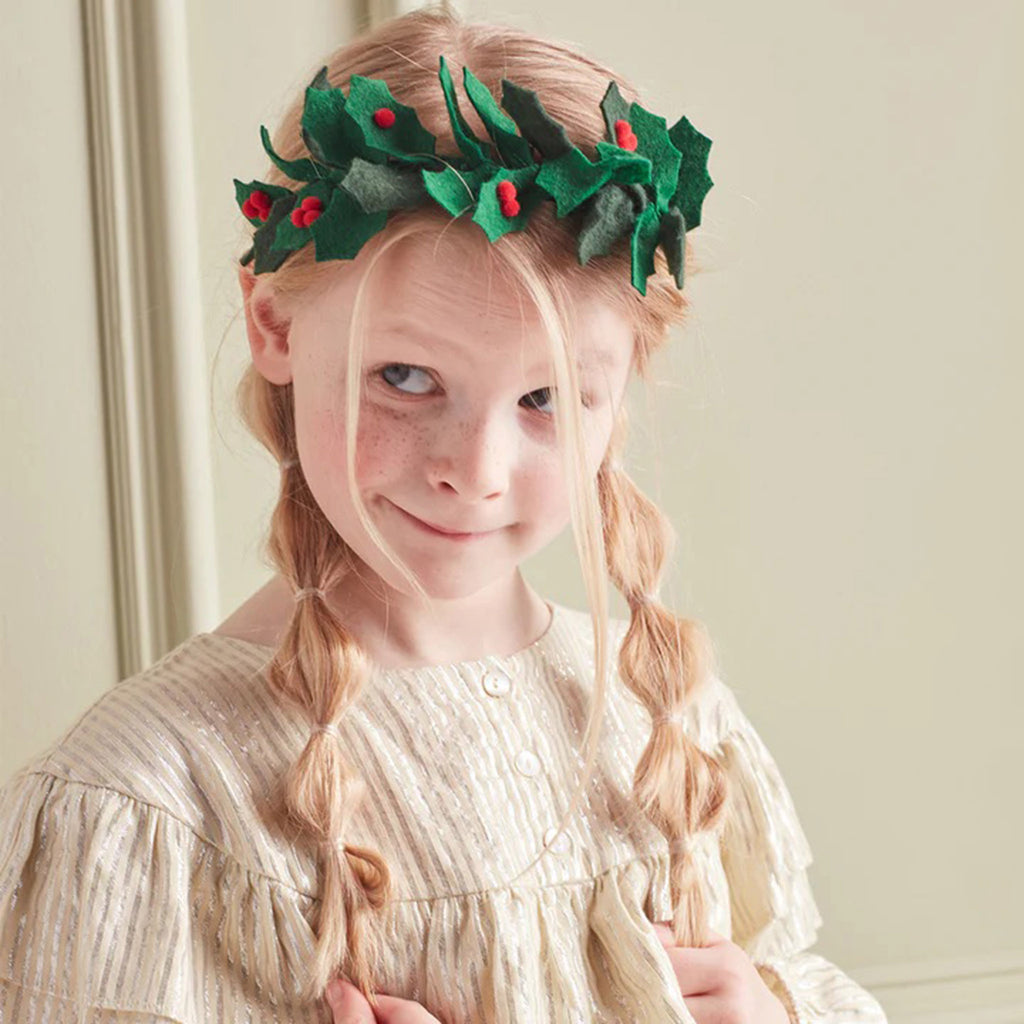 Green gingham ribbon headband with green felt holly leaves and red pompom holly berries attached being worn by a child.