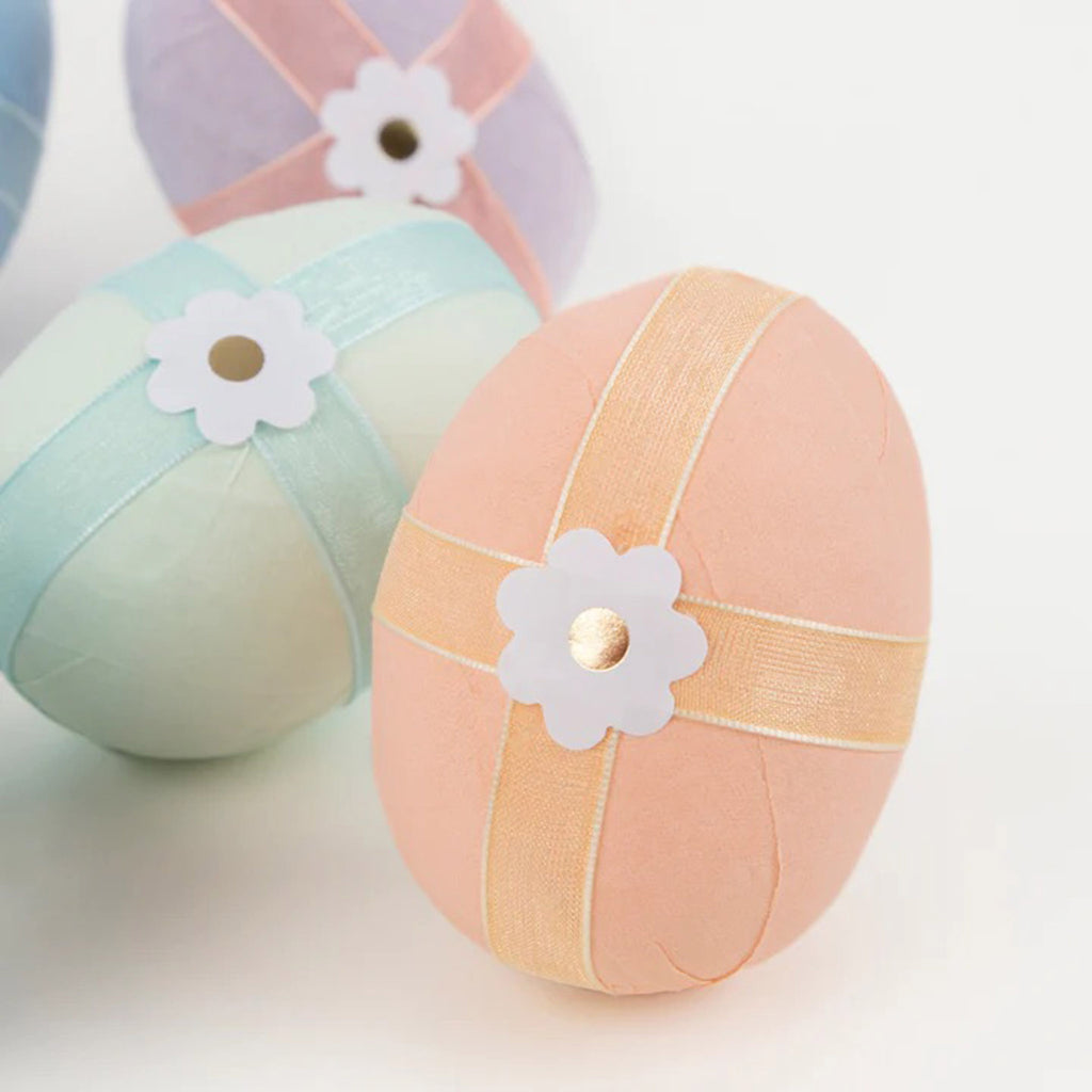 Detail of a Meri Meri crepe paper wrapped surprise egg in peach crepe paper with orange organza ribbon and daisy sticker.
