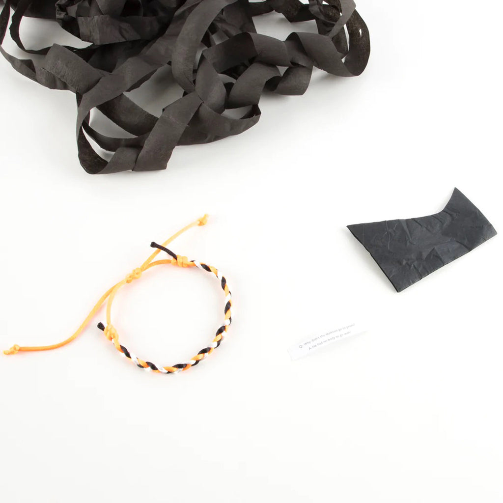 Spider shaped surprise ball contents including a black paper hat; an orange, white and black friendship bracelet and a joke.