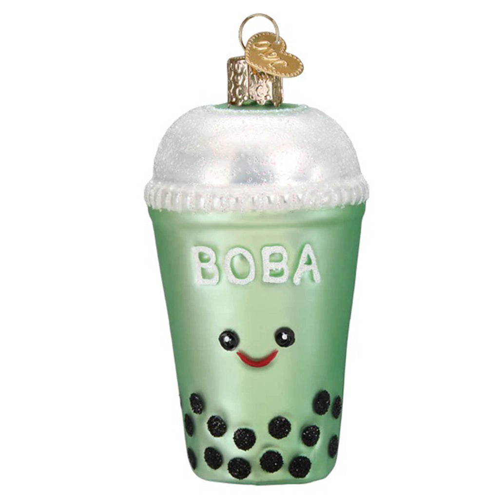 Front view of a glass holiday ornament that looks like a cup of green boba tea with black eyes and a red smile, black beads at the bottom and a white bubble cap.