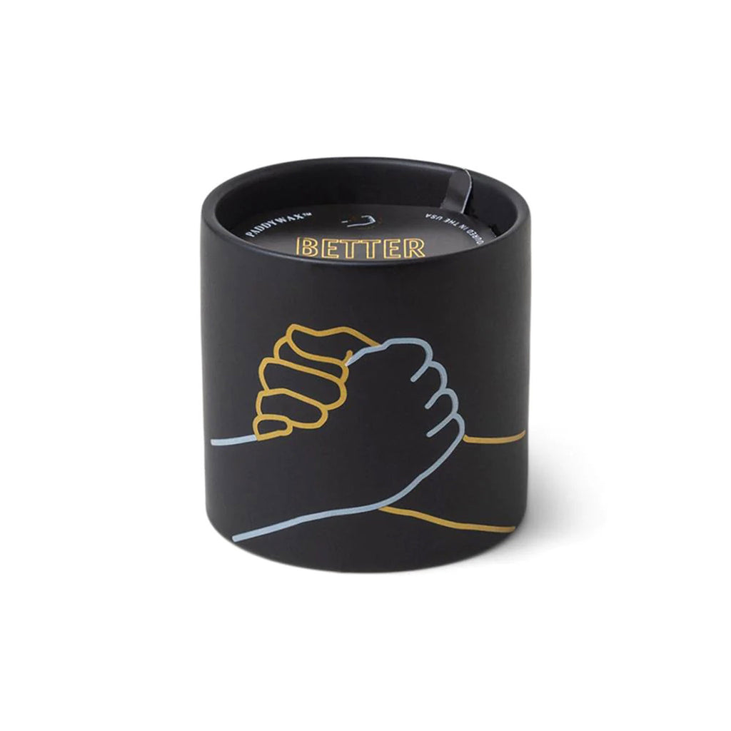 paddywax impressions 5.75 ounce hands shaking better together incense and smoke scented soy wax candle in matte black ceramic vessel.