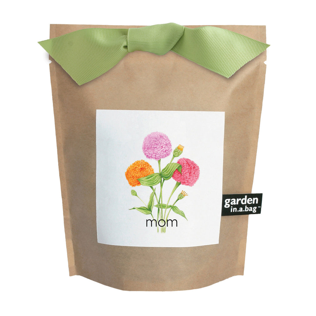Potting Shed Creations Mom Garden in a Bag, front of waxed kraft paper bag with green grosgrain ribbon bow and label with an illustration of a orange, pink and purple dwarf zinnia flowers.