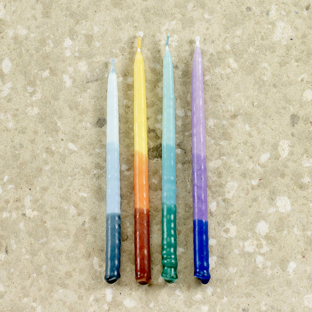 Pure natural vegetable wax Hanukkah menorah candles with a tri-color ombre design on a stone background. Colors are blue, orange, green and purple.