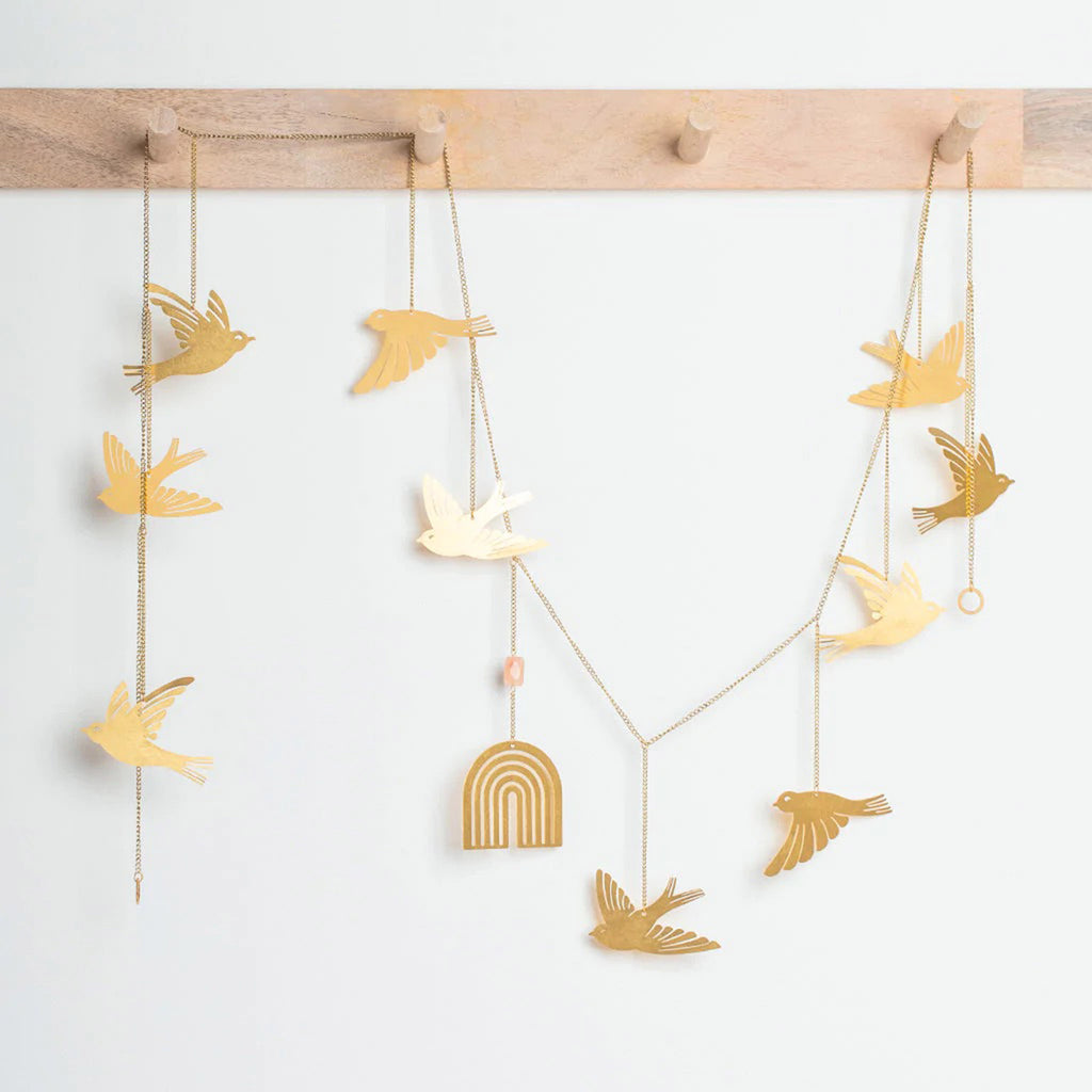 Brass hanging garland home decoration with various birds in flight and a rainbow, strung out on wooden pegs.