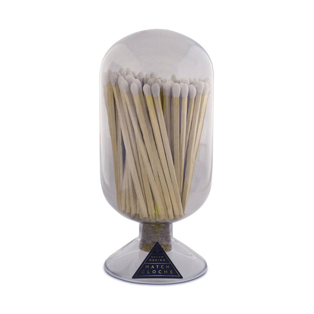 Vertical oblong oval shaped smoke gray glass vessel with circular base and filled with white tipped wood safety matches on a white background.