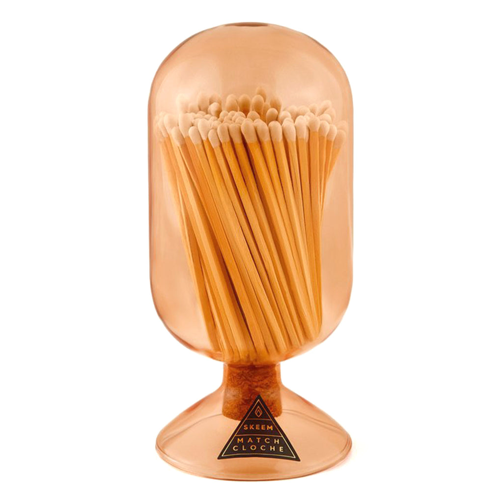 Vertical oblong oval shaped apricot peach glass vessel with circular base and filled with white-tipped wood safety matches on a white background.