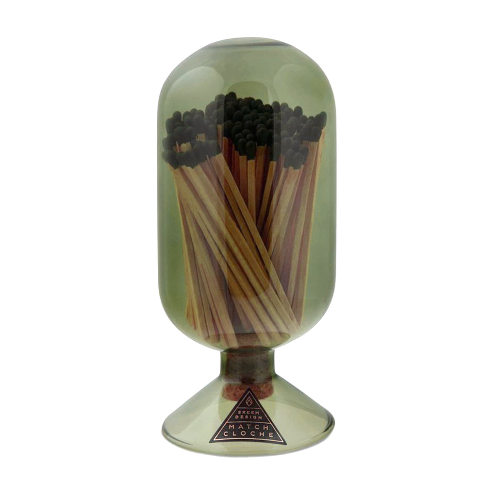 Vertical oblong oval shaped olive green glass vessel with circular base and filled with black-tipped wood safety matches on a white background.