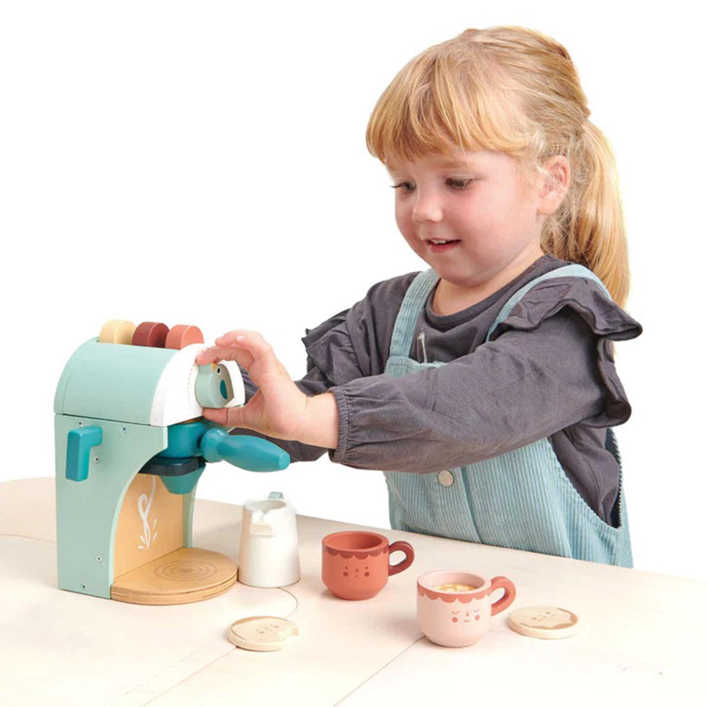 Child playing with the Tender Leaf Toys Wooden Babyccino Maker kids toy that looks like a cappuccino machine.