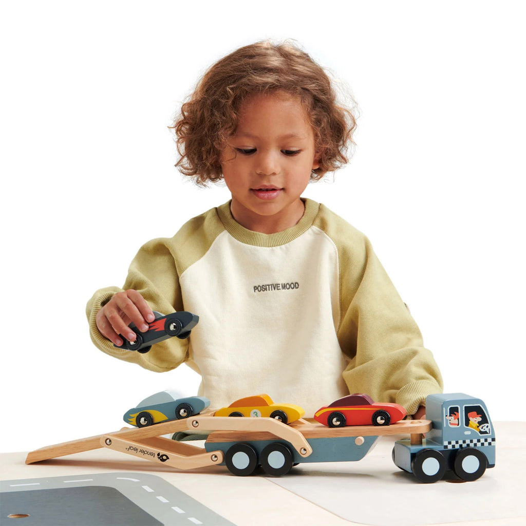 Wooden car transporter truck with 4 wooden sports cars, there is a child placing the cars on the extended truckbed.