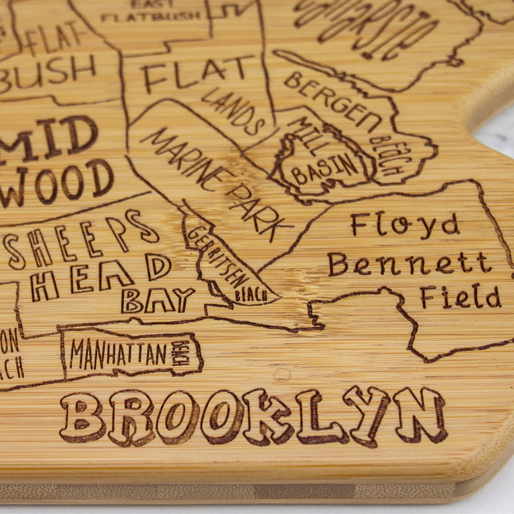 Brooklyn shaped bamboo serving board that is laser engraved with the neighborhood shapes and names and "brooklyn" at the bottom, close-up detail shot.