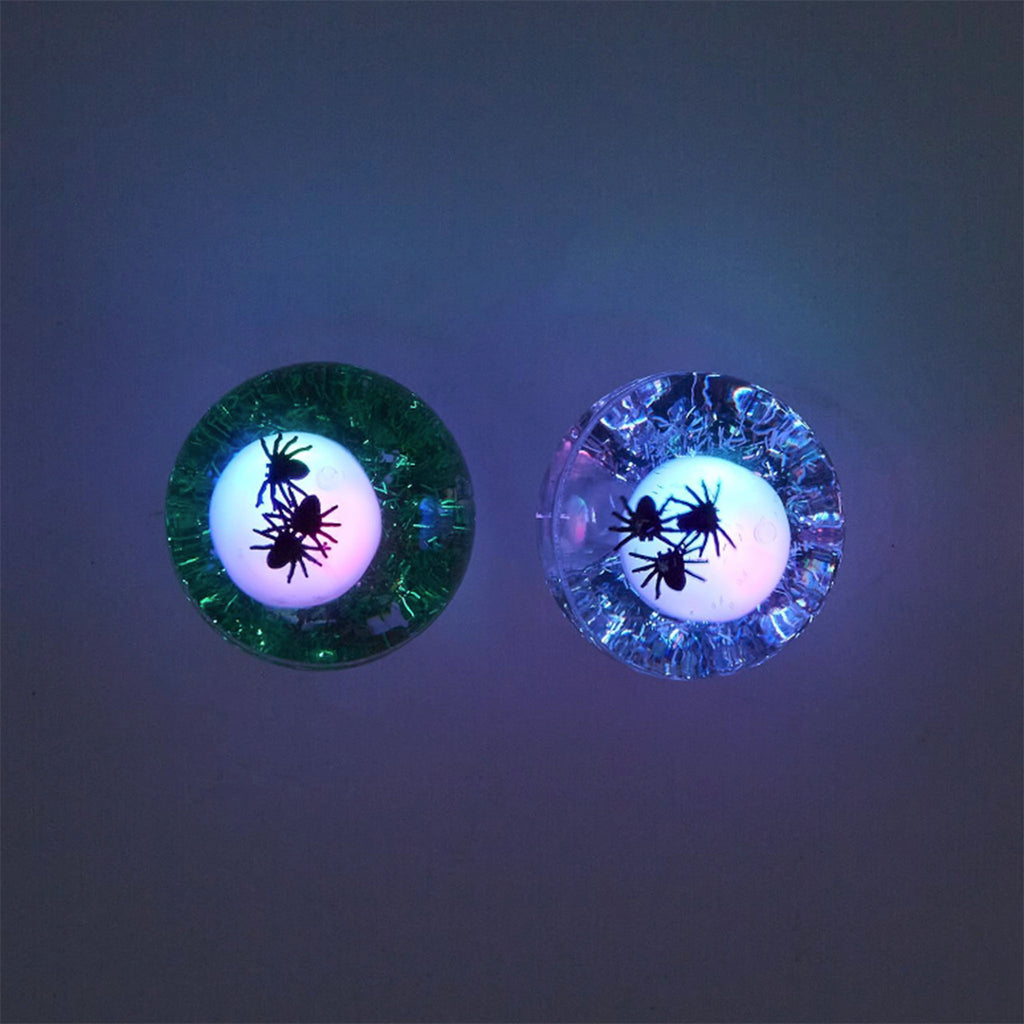 Top view of rubber bouncing balls with a light up skull, little black spiders and green or silver glitter on a black background in the dark.