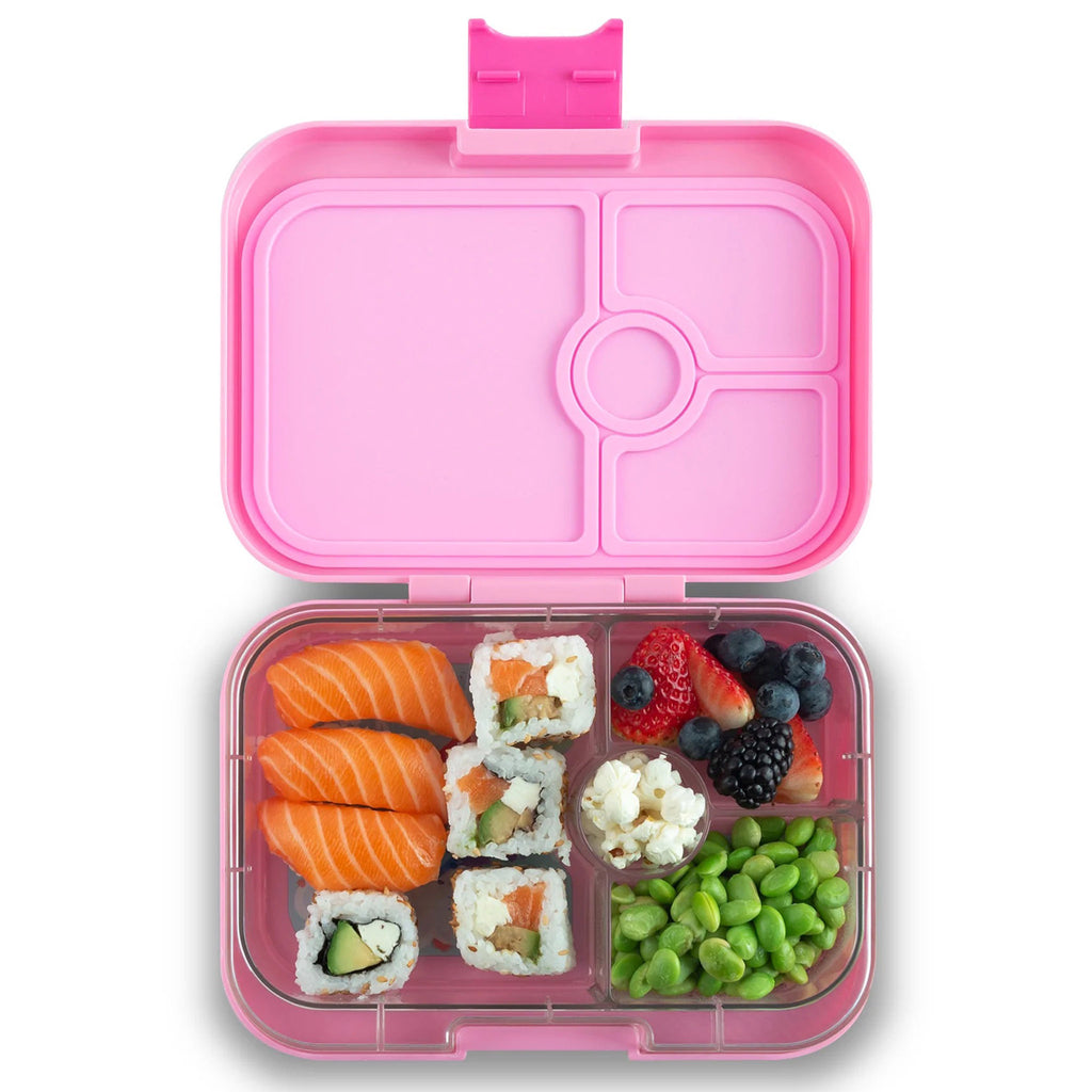 yumbox lunch box in pink, lid open showing clear inner tray divided into 4 compartments with salmon sashimi, 4 pieces of sushi, popcorn, mixed berries and shelled edamame