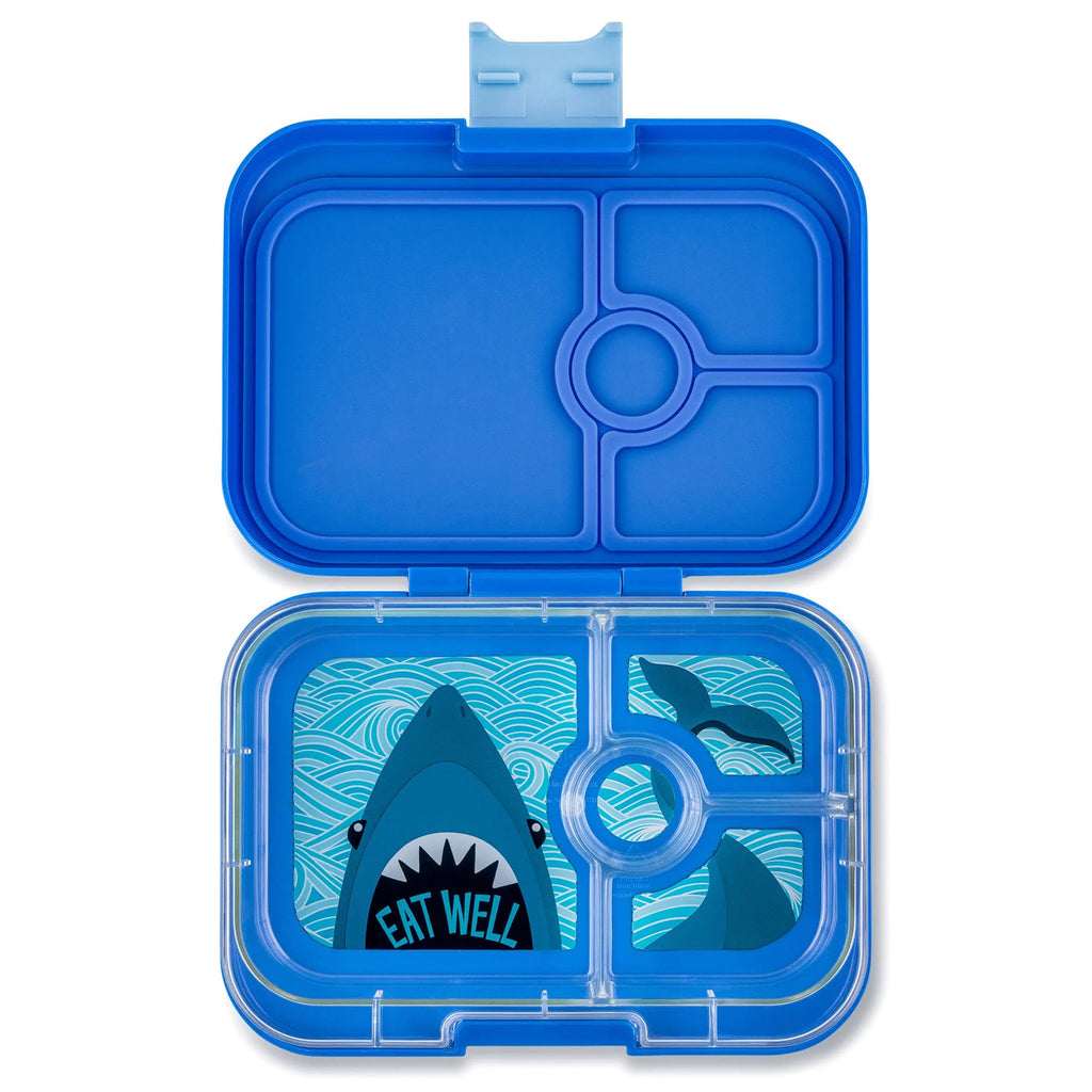 yumbox lunch box in royal blue, lid open showing clear inner tray divided into 4 compartments with an illustration of a shark head in large compartment with "eat well" in its mouth and rest of its body and tail illustrated in smaller compartments to the right